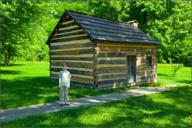 Holden (in photo for scale) standing in front of the reconstructed boyhood cabin of Abraham Lincoln at Knob Creek